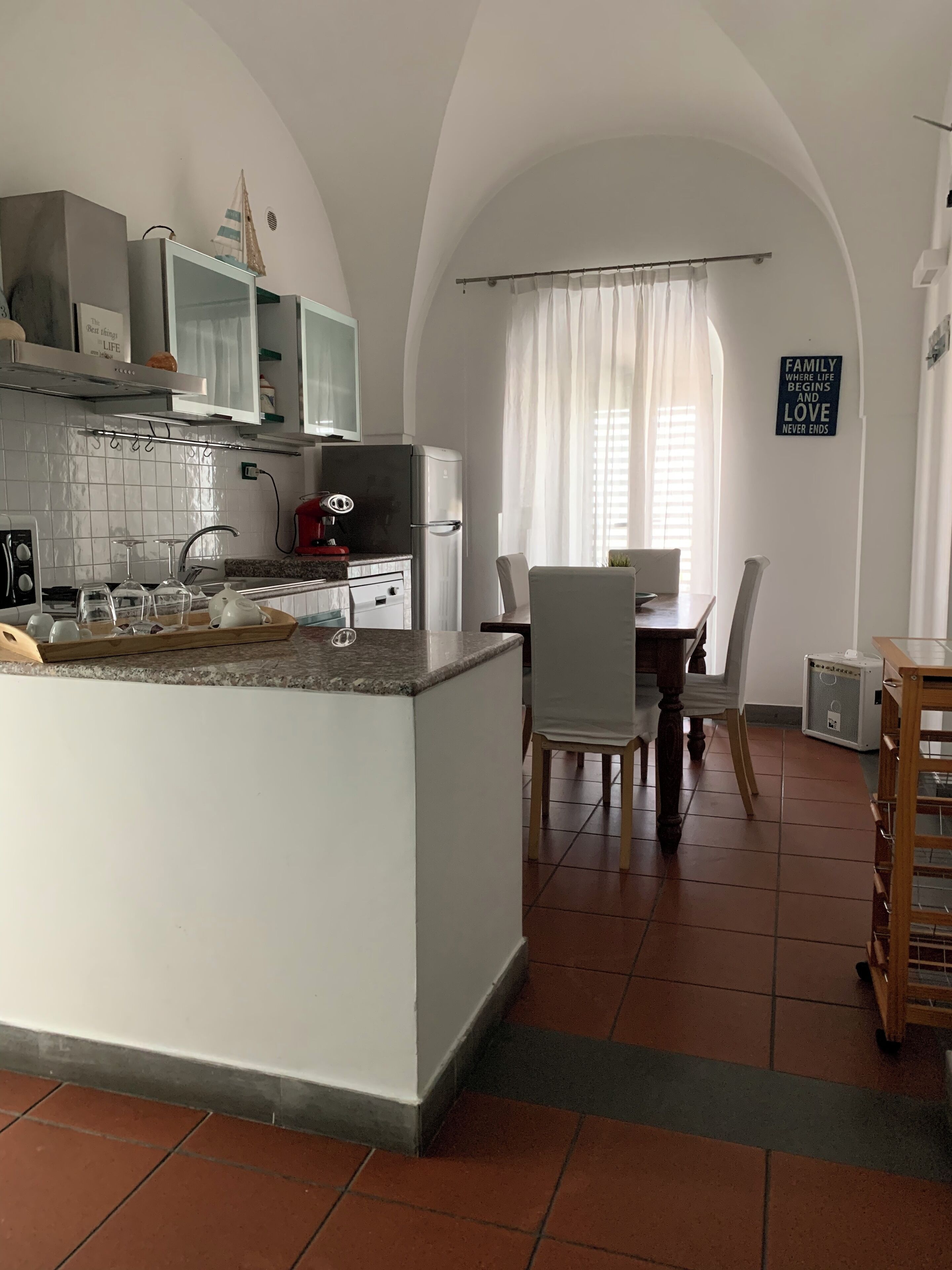 Una cocina con una isla central, armarios blancos y un comedor con mesa y sillas.