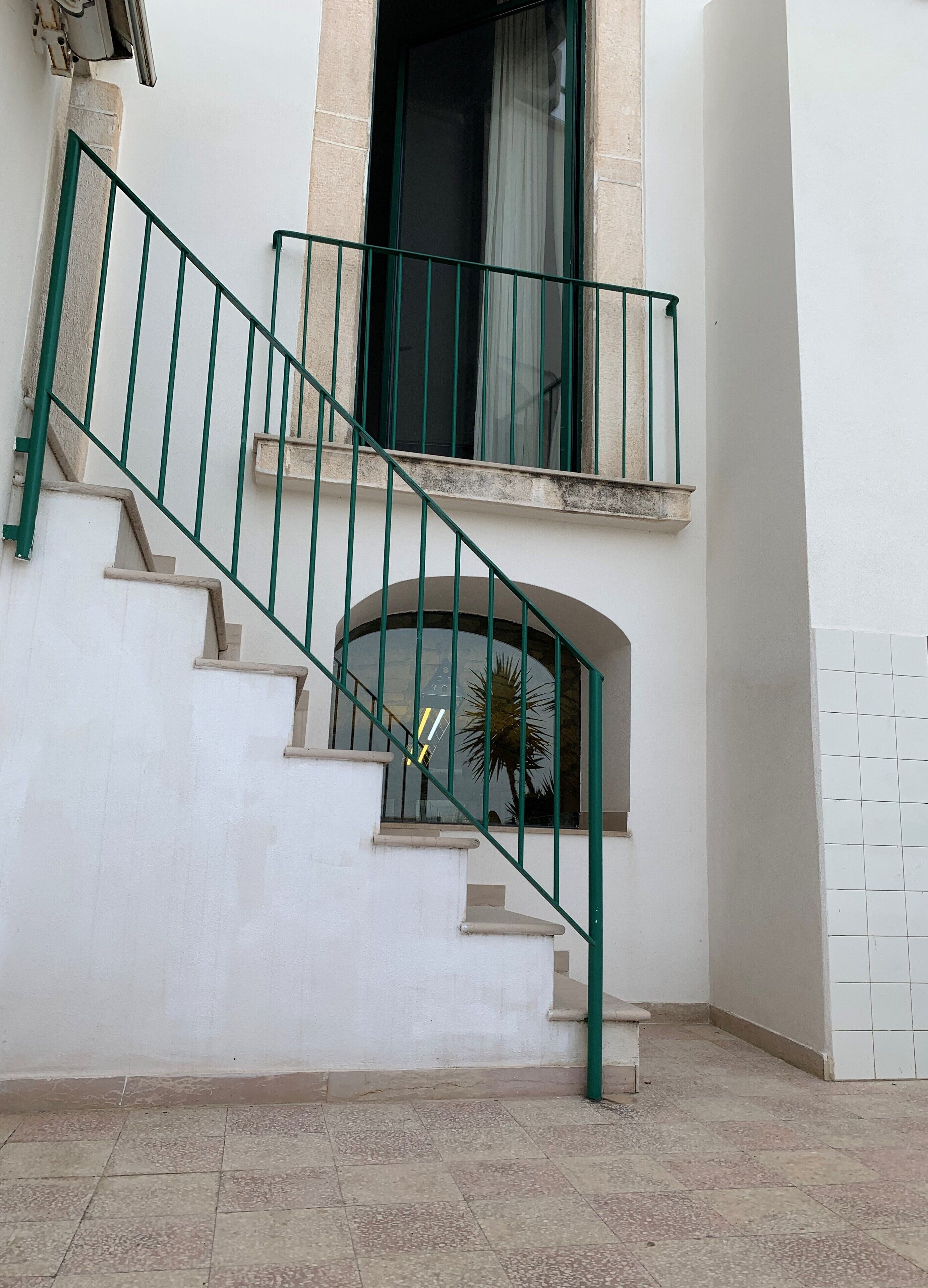 Una escalera con barandillas verdes que lleva a un rellano con una ventana.