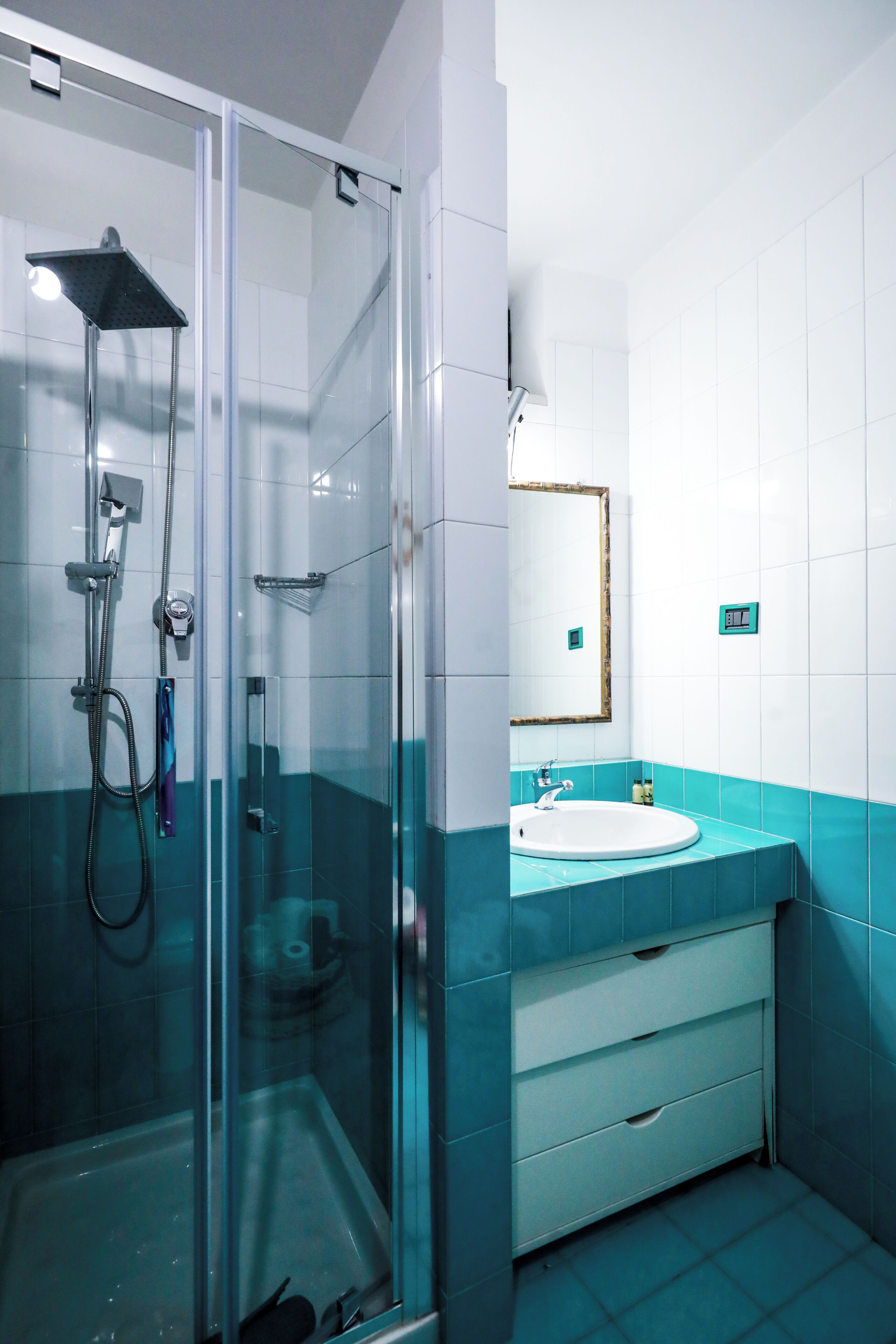 Une salle de bain moderne avec une douche à parois de verre, un lavabo blanc doté d’un plan de travail bleu et un miroir avec un cadre en bois.