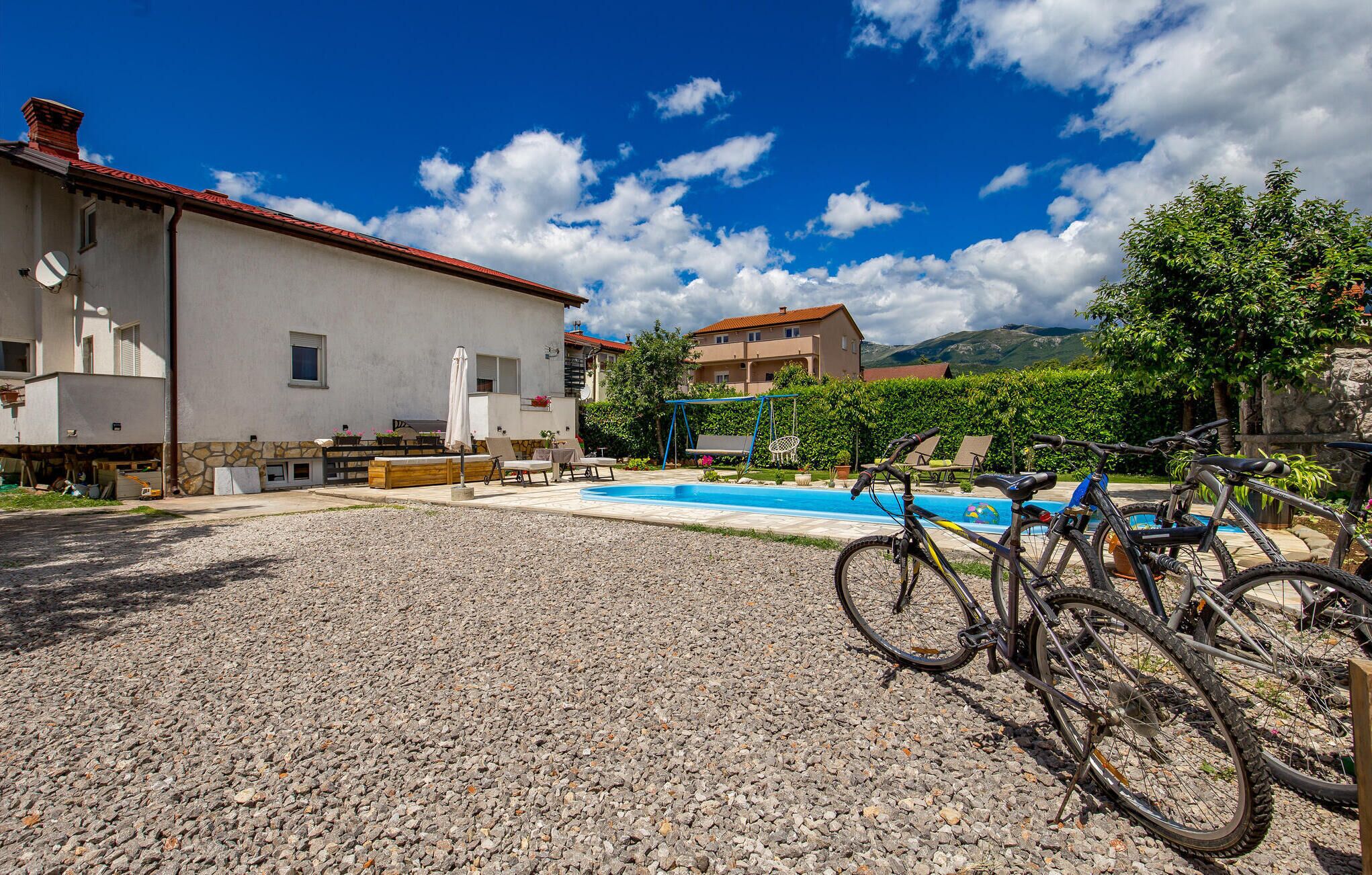 A pool area with a gravel surface, a swing set, and bicycles parked near the pool.
