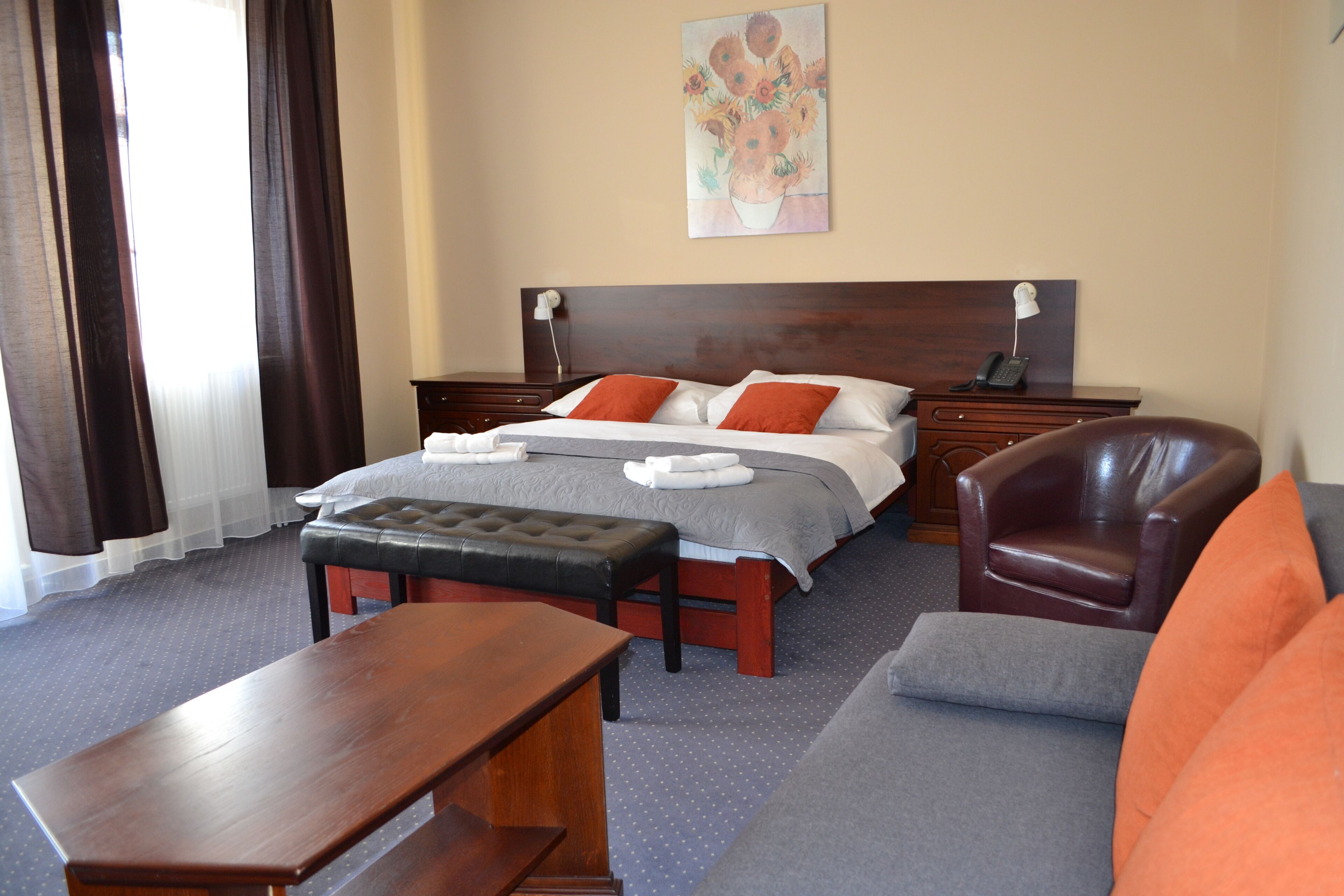 A hotel room with a bed, a wooden bench, a sofa, a chair, and a desk.