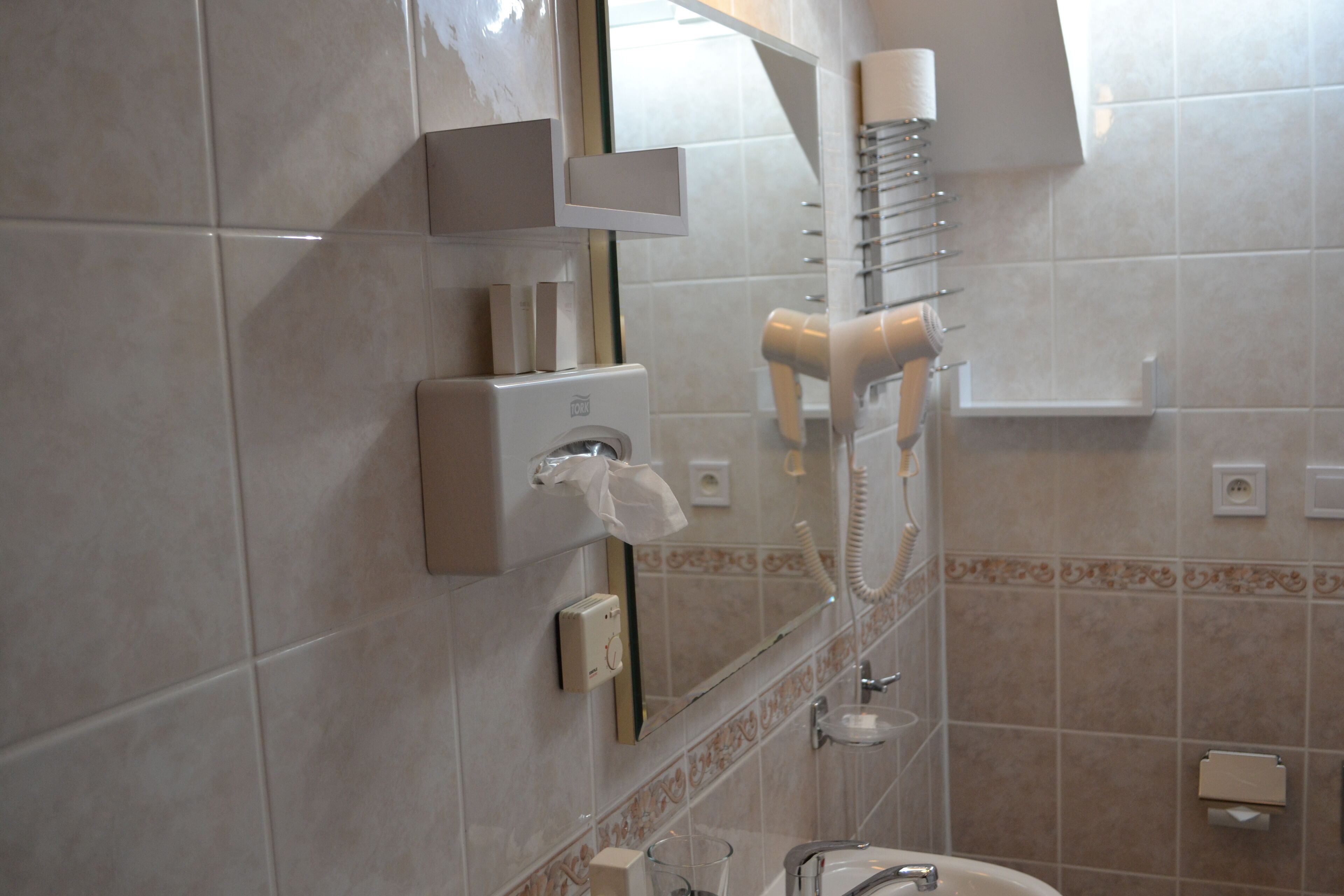 Un baño con un secador de pelo montado en la pared, un dispensador de toallas y un espejo.