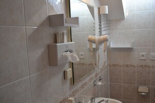 Un baño con un secador de pelo montado en la pared, un dispensador de toallas y un espejo.