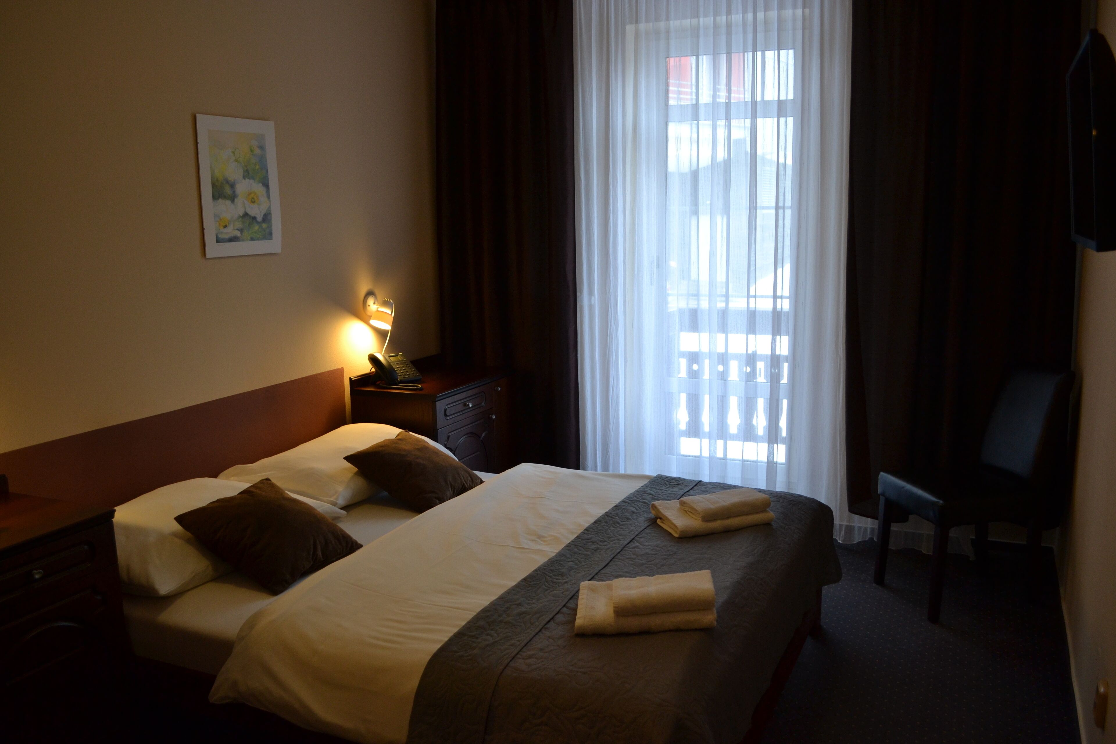 A hotel room with a bed, a nightstand, a chair, and a window with curtains.