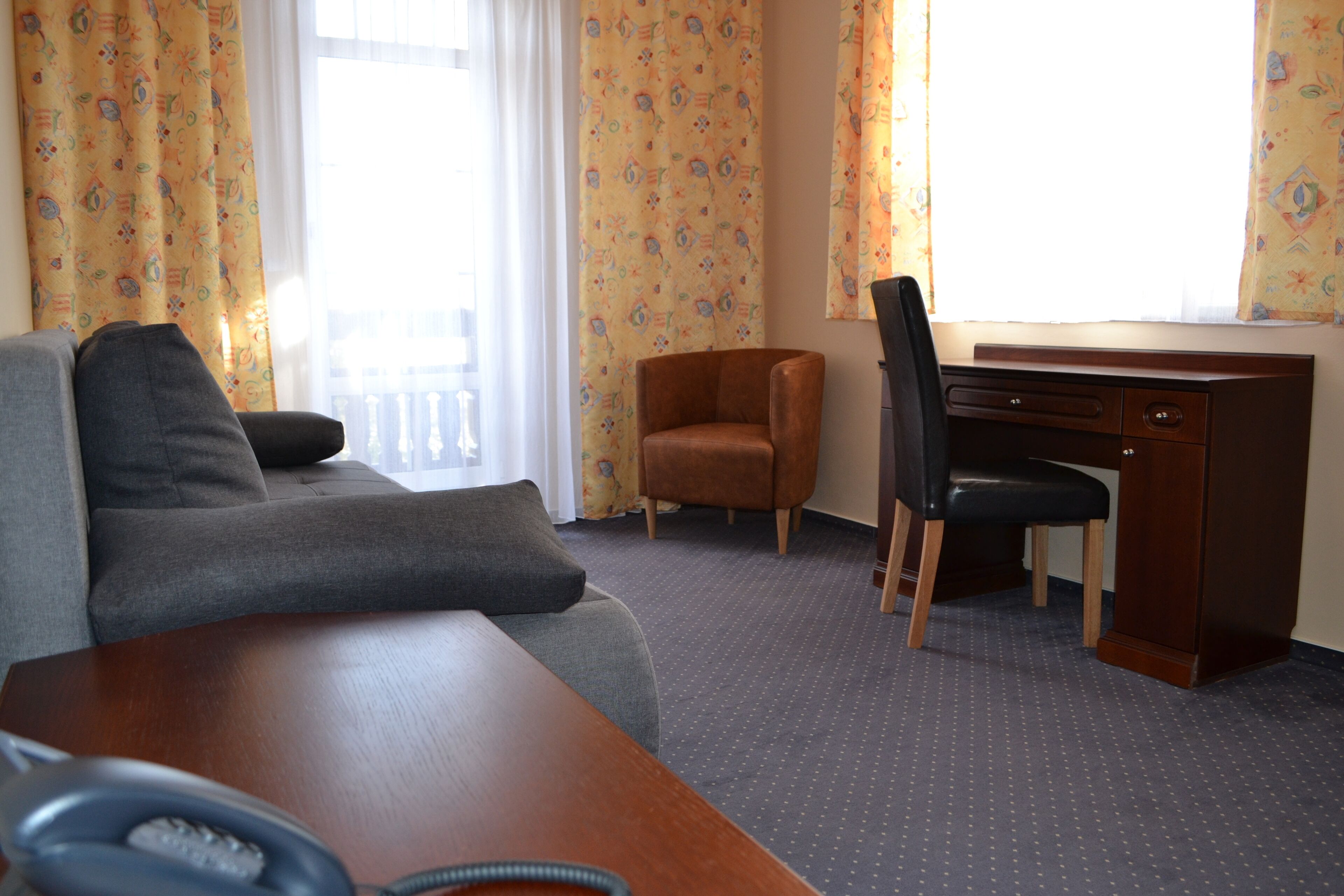 Quarto de hotel com sofá, escrivaninha, cadeira e telefone.