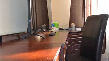 A hotel room with a wooden desk, a black office chair, a mirror, and a window with curtains.