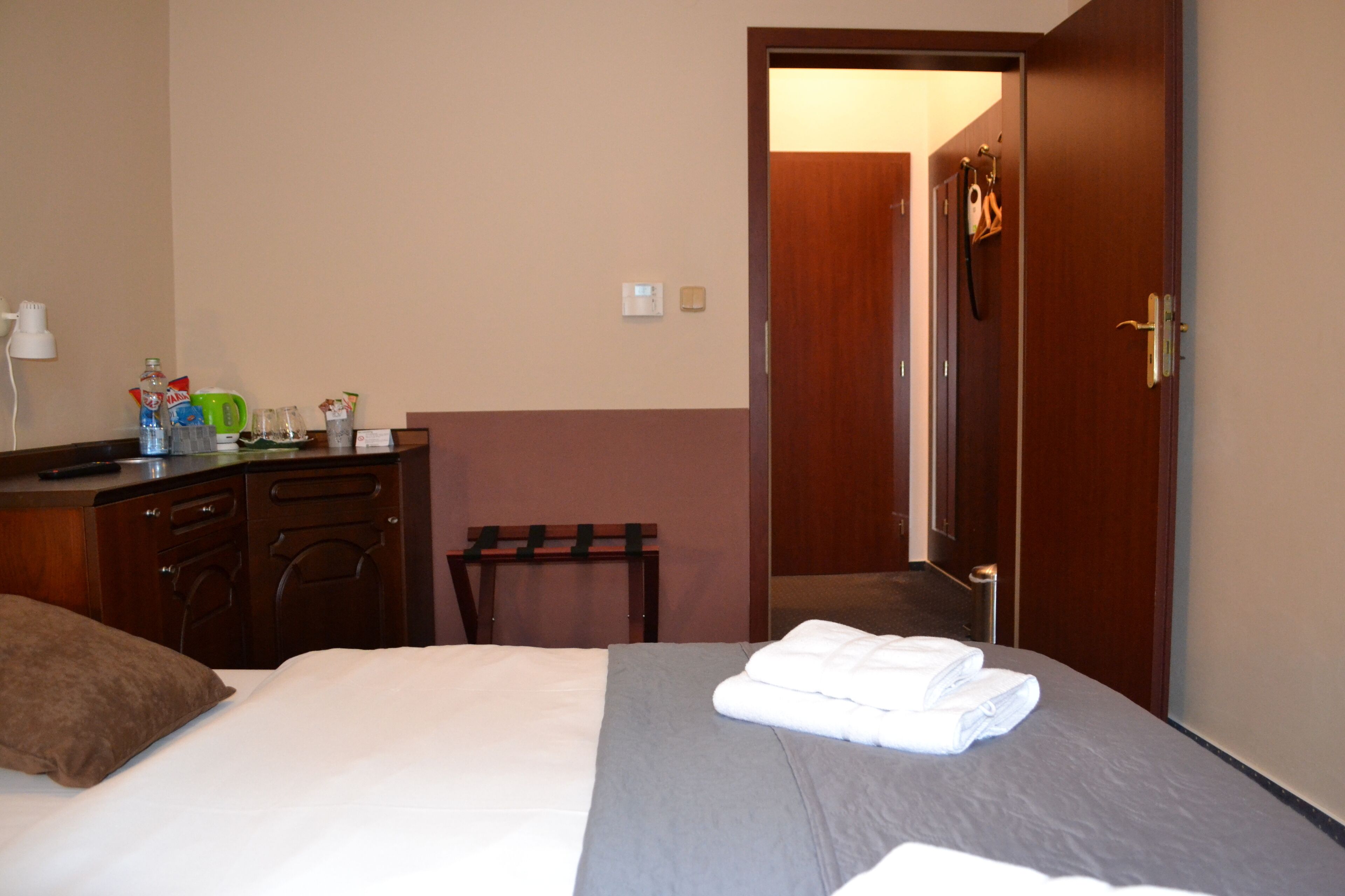 A hotel room with a bed, a wooden dresser, a small table, and a door leading to another room.