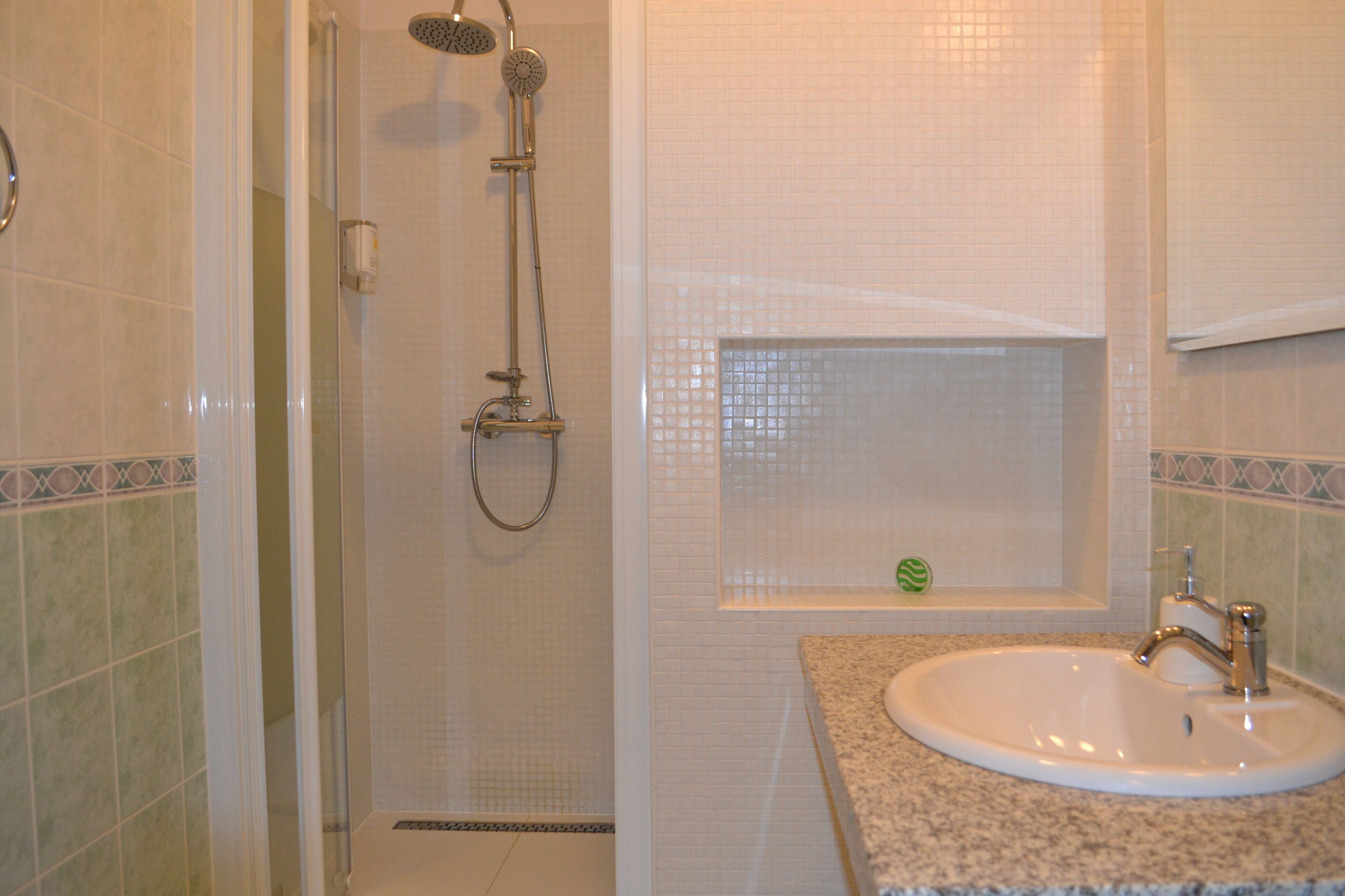 A bathroom with a shower, a sink, and a small window with a decorative item.