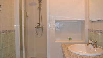 A bathroom with a shower, a sink, and a small window with a decorative item.