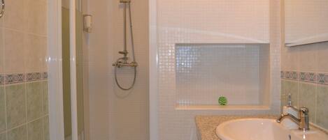 A bathroom with a shower, a sink, and a small window with a decorative item.
