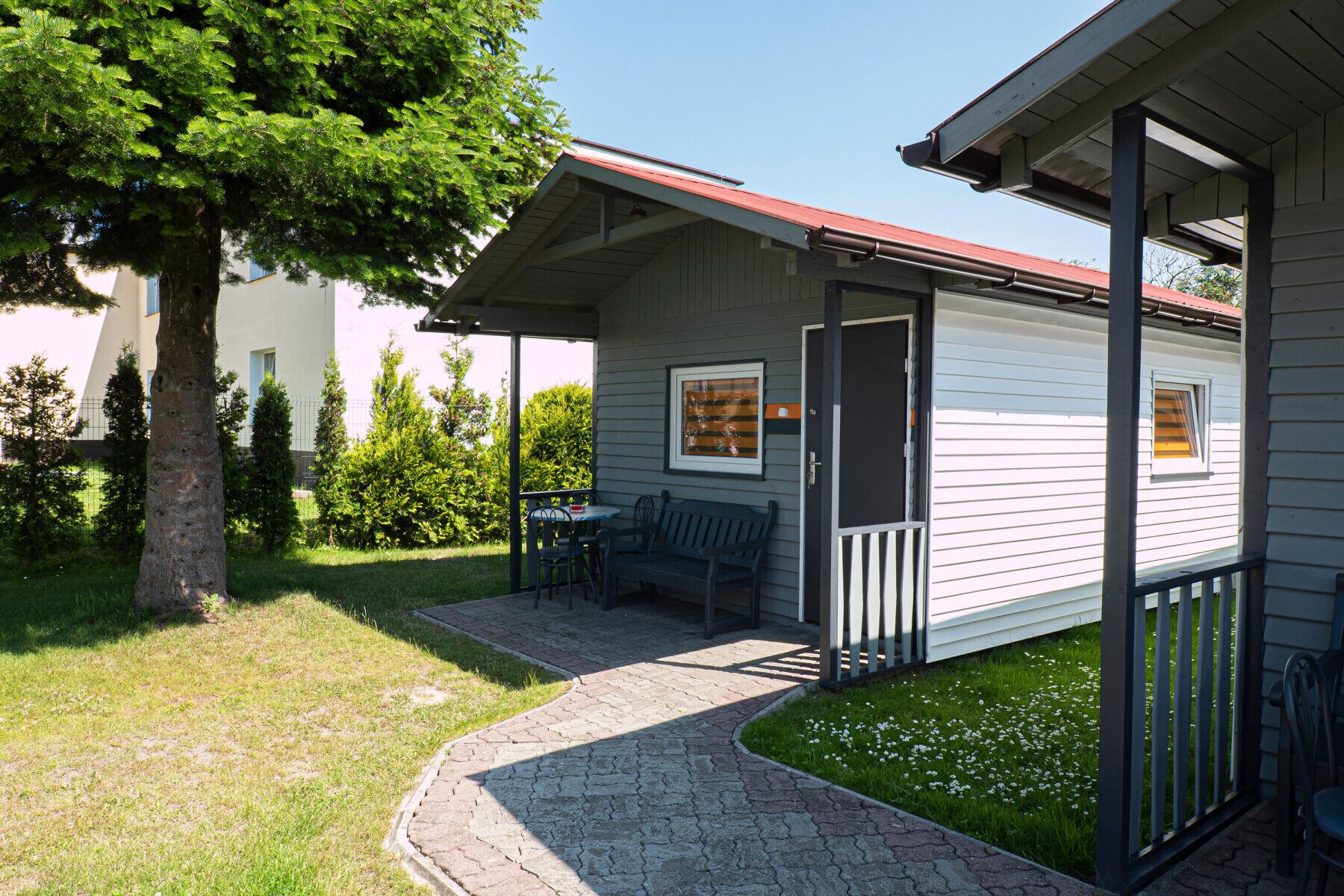 A small, single-story building with a covered porch, a bench, and a table.