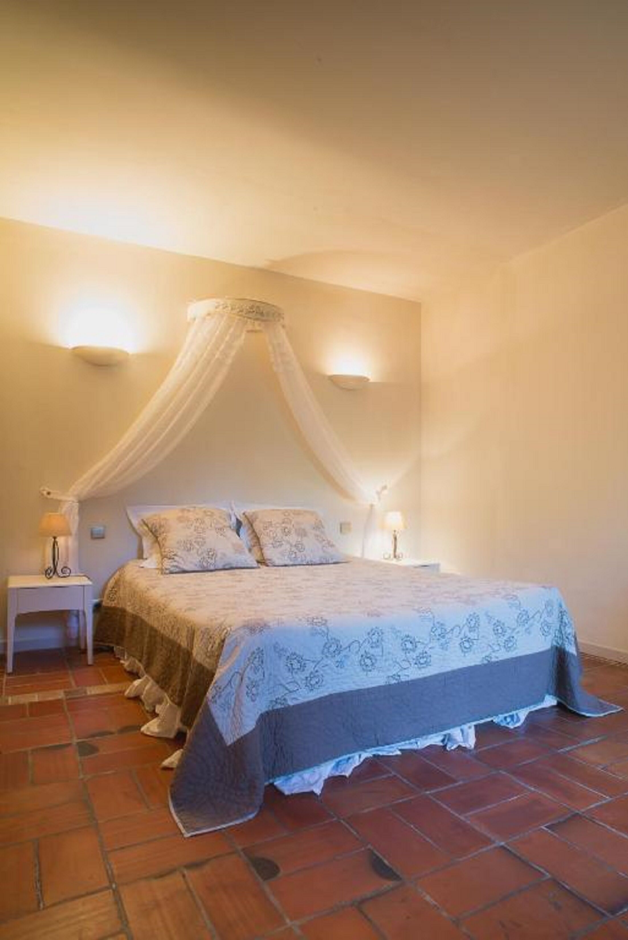 A bedroom with a canopy bed, two bedside lamps, and a tiled floor.