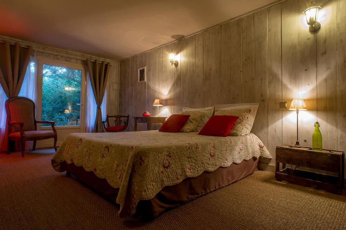 A cozy bedroom with a large bed, two bedside lamps, a chair, and a small table.