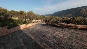 A stone pathway leading through a landscaped area with trees and a view of distant hills.