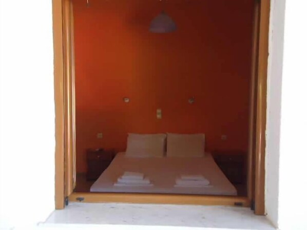 Una habitación con una cama, dos almohadas, una mesita de noche y una lámpara colgante.