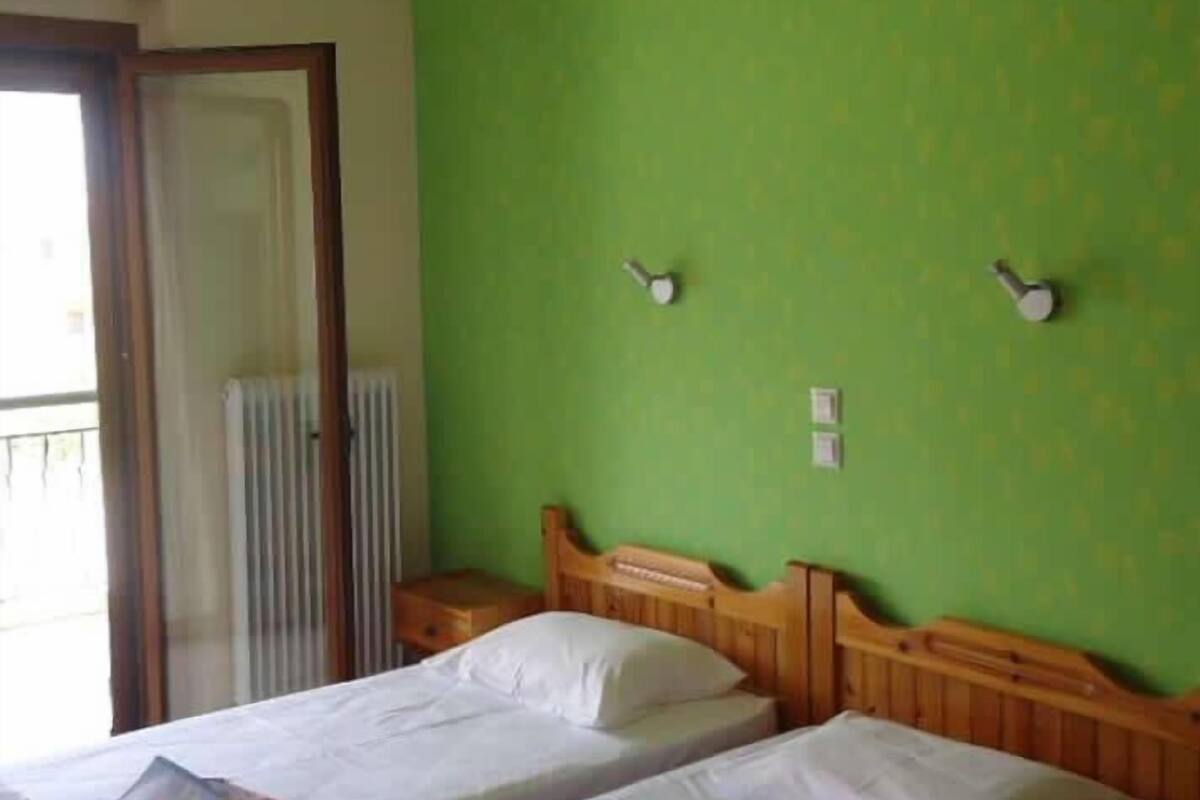 A room with two single beds, a wooden headboard, a radiator, and a green wall.
