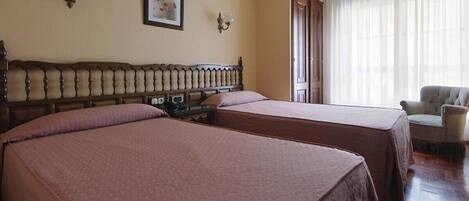 Habitación de hotel con dos camas, cabecera de madera, televisor y una silla.