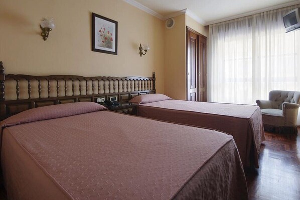 A hotel room with two beds, a wooden headboard, a television, and a chair.