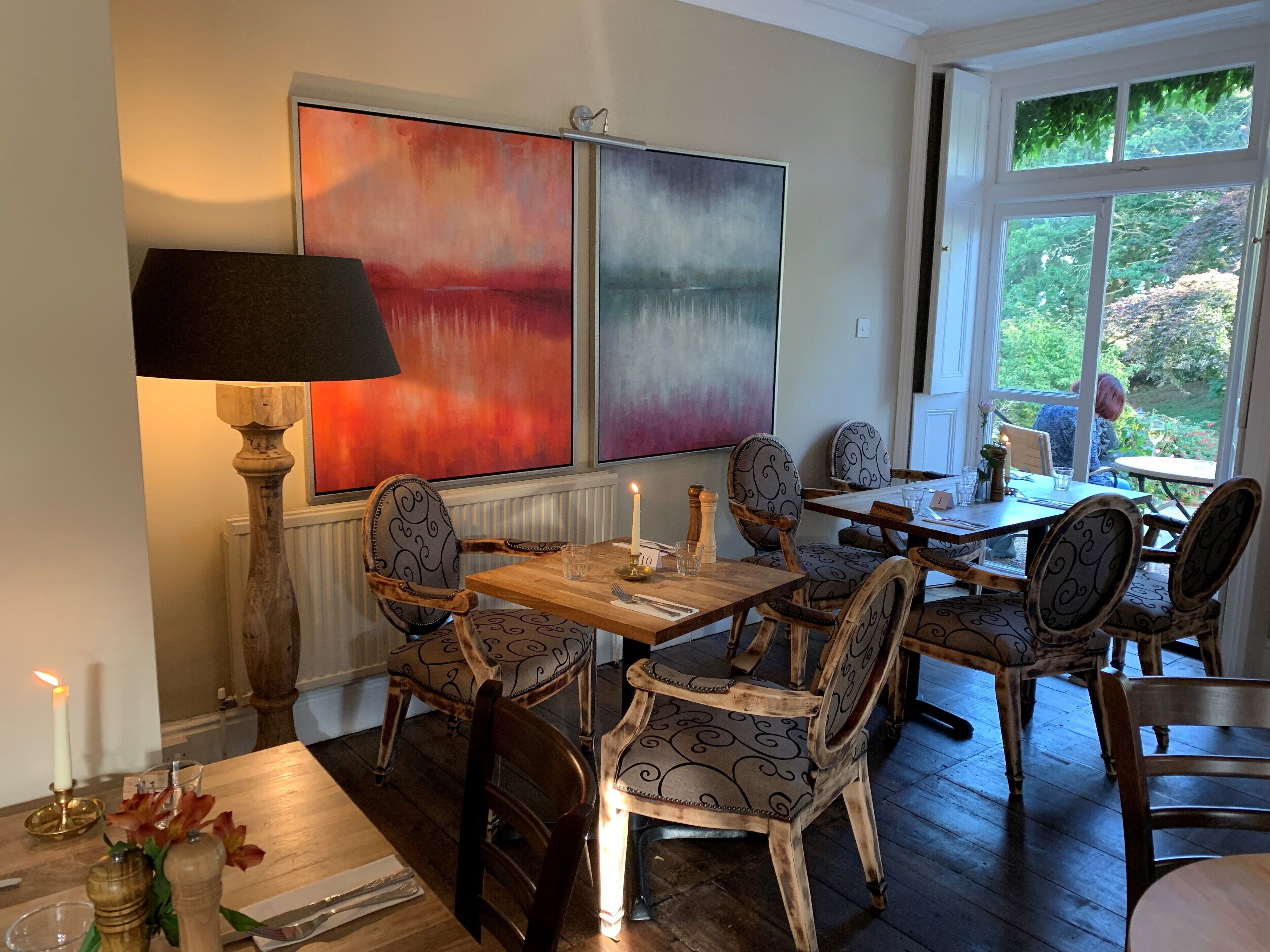A dining area with a wooden table and chairs, a floor lamp, and abstract paintings on the wall.