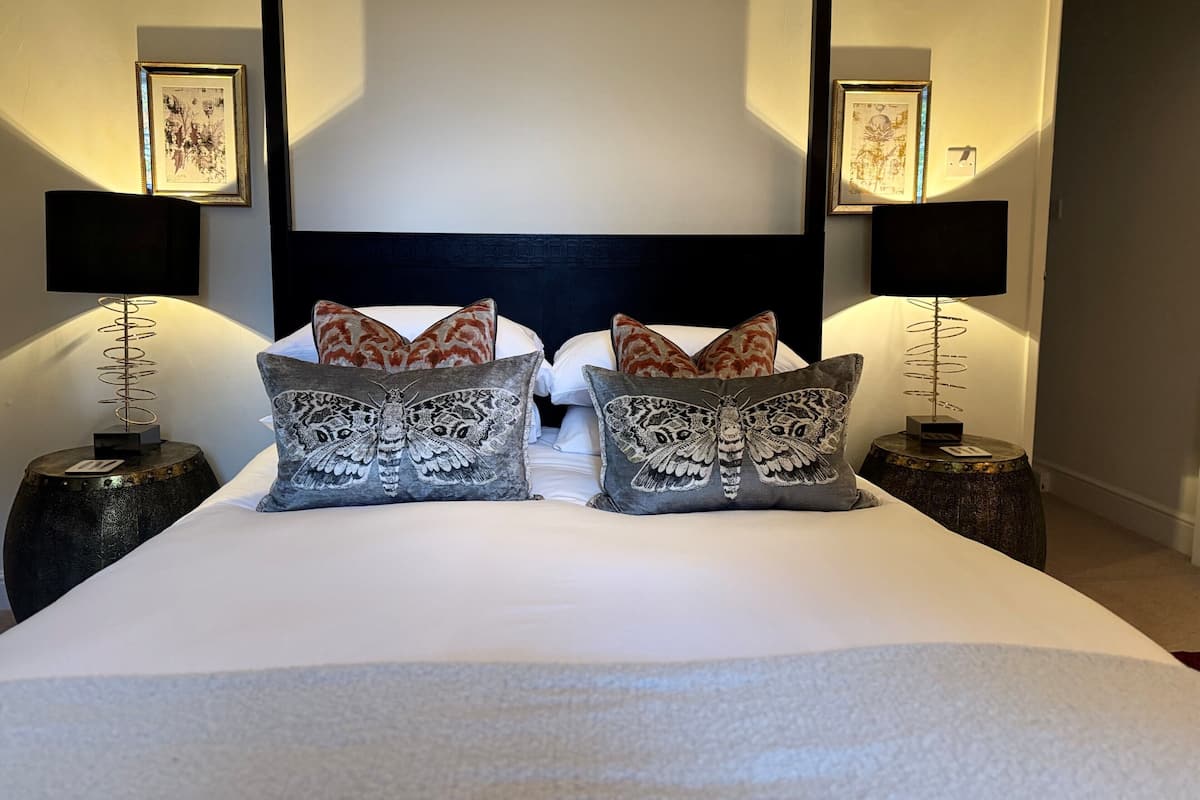 A neatly made bed with two pillows and a headboard, flanked by two bedside tables with lamps and framed pictures.
