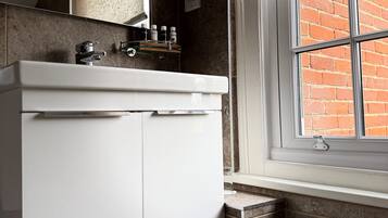 Un baño con un lavabo blanco, un espejo y una ventana que da a un edificio de ladrillo.