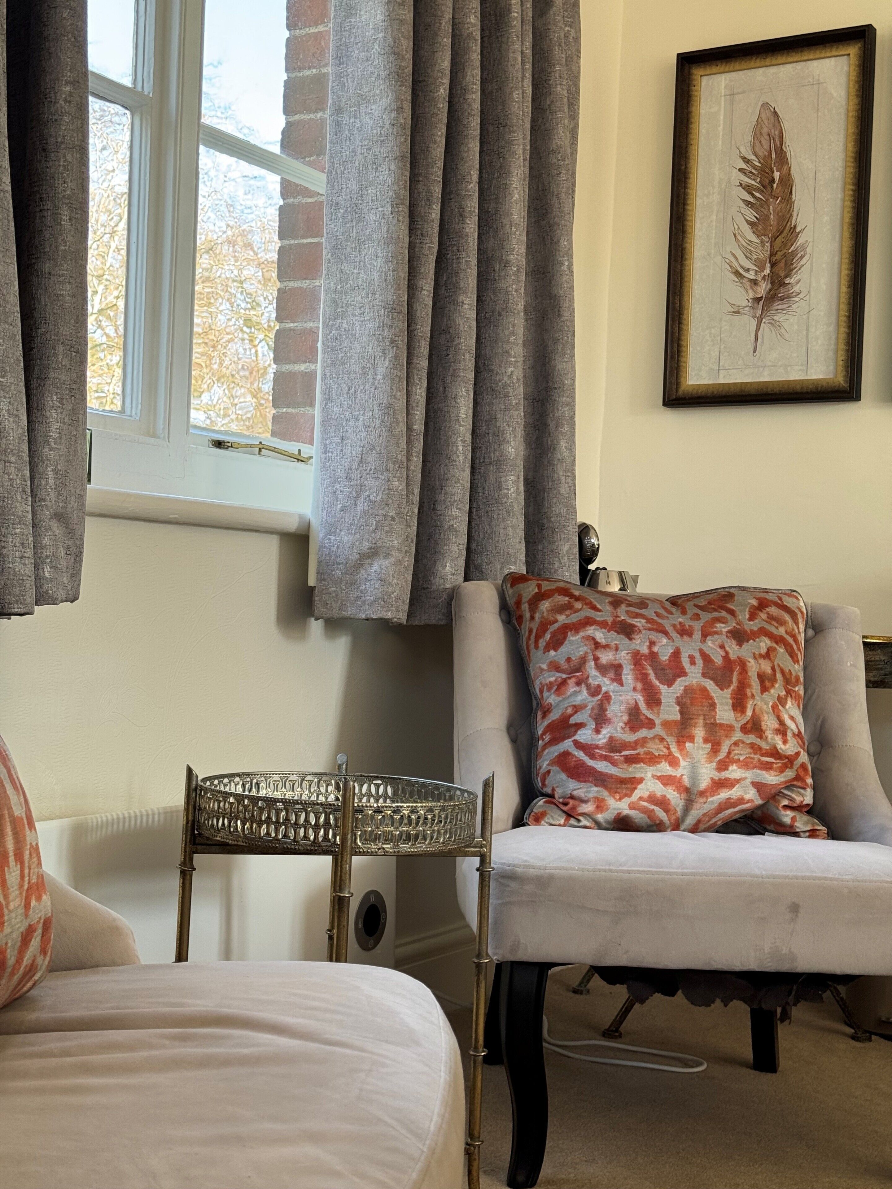 A room with a bed, a chair, a window with curtains, a radiator, and a framed picture on the wall.