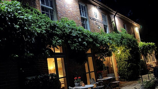 A brick building with a sign reading "CANTERBURY HILL" at night, outdoor seating with tables and chairs, and a gravel path. - Scarborough Hill Country Inn (North Walsham)