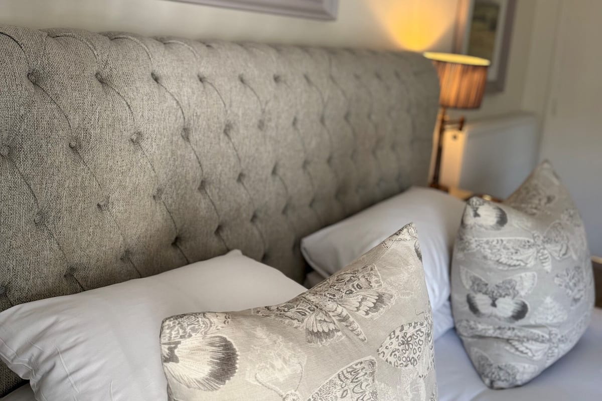 A bed with a tufted headboard, patterned pillows, and a framed landscape painting above.