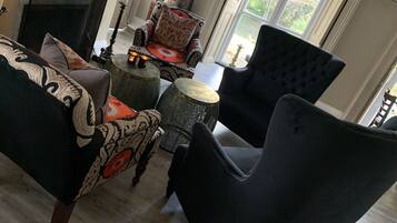 Un salon doté d’une cheminée, de fauteuils à motifs et d’une grande fenêtre donnant sur un paysage verdoyant.