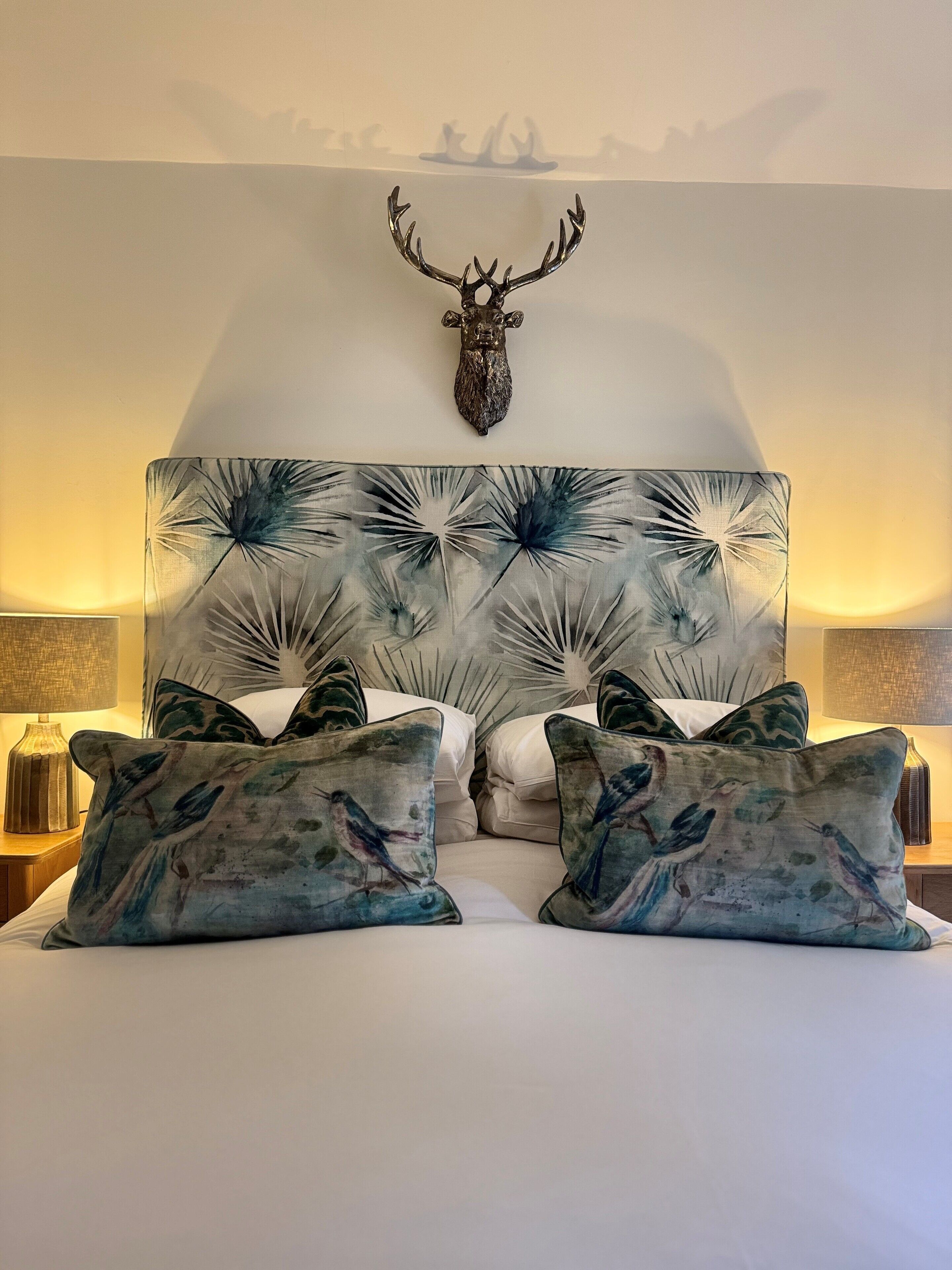 A bed with a decorative headboard featuring a bird pattern, flanked by matching pillows, and a mounted deer head above.