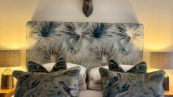 A bed with a decorative headboard featuring a bird pattern, flanked by matching pillows, and a mounted deer head above.