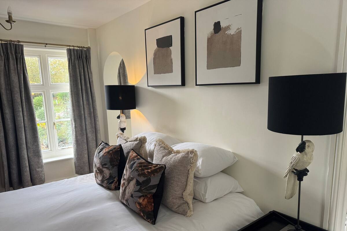 A bedroom with a bed, pillows, a nightstand, a lamp, and artwork on the wall.