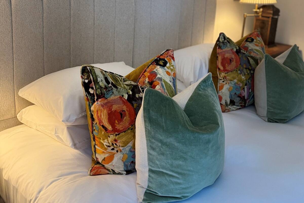 A neatly made bed with white linens and multiple pillows, including a floral one and a solid green one.