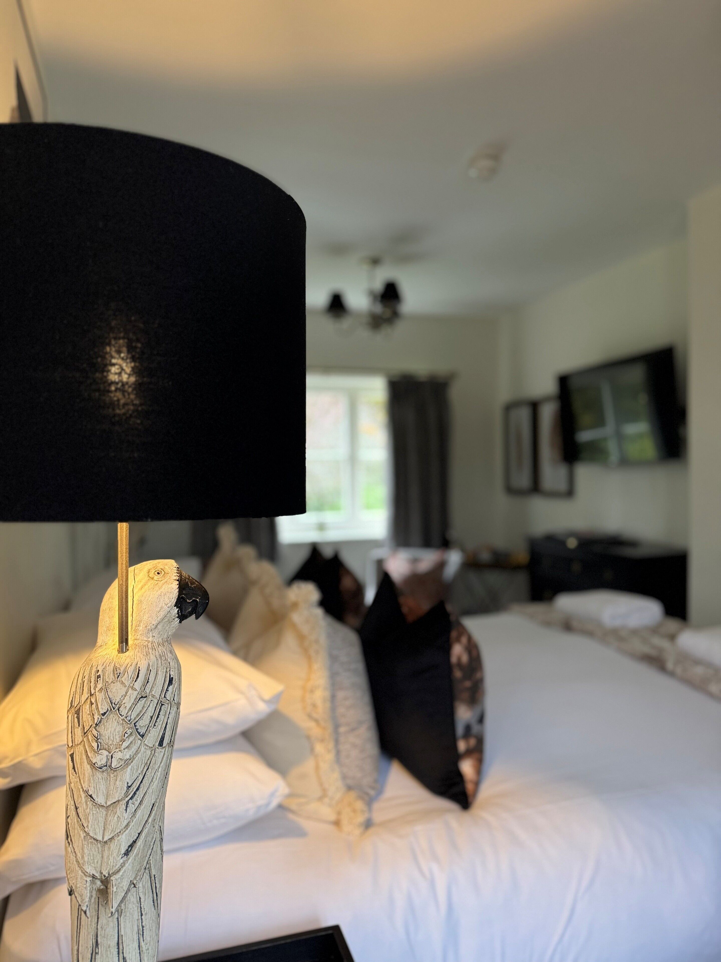 A room with a bed, pillows, a lamp, and a television on the wall.