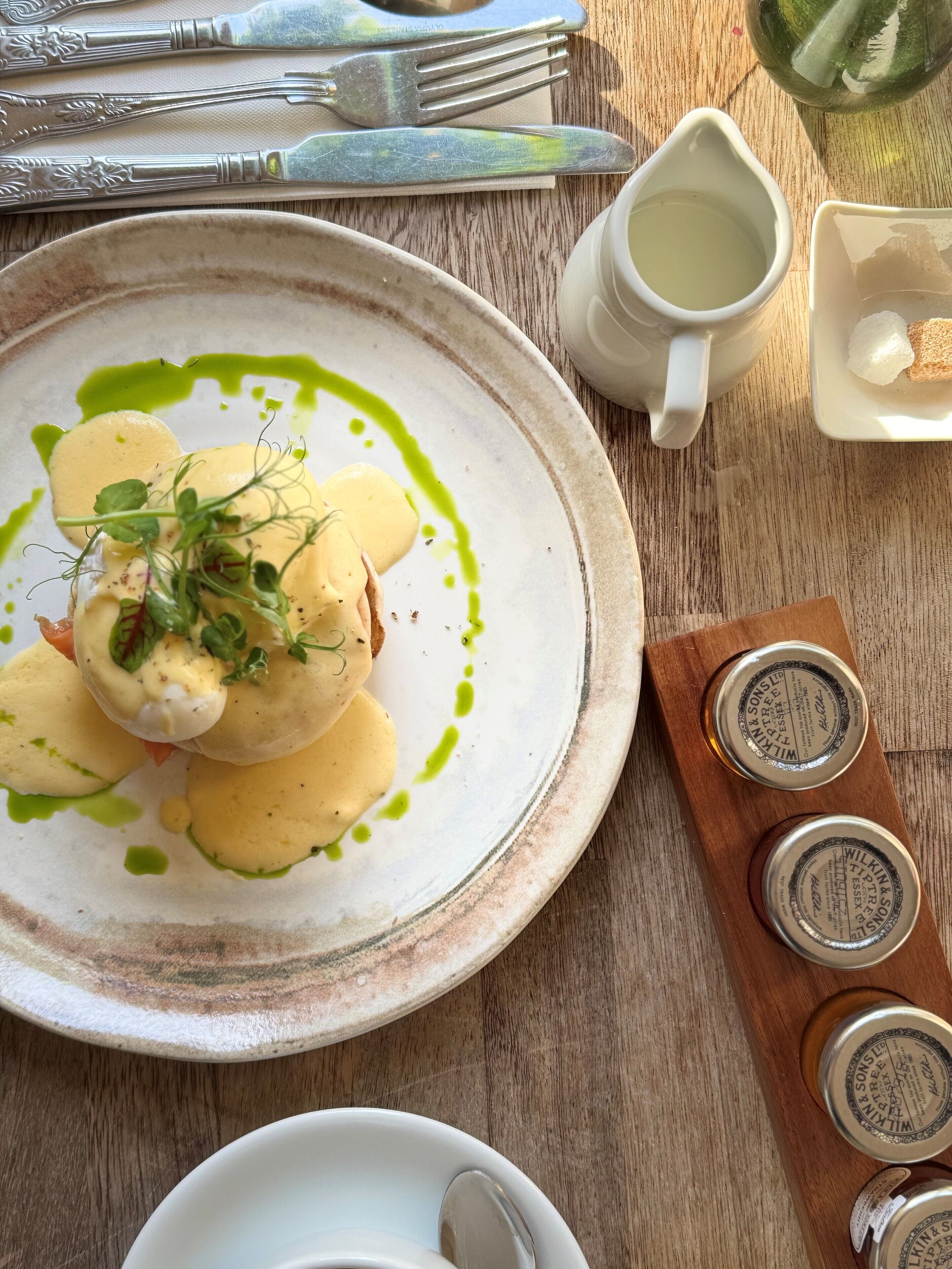 A plate of food with a green sauce, a white cup, and a wooden tray with jars.