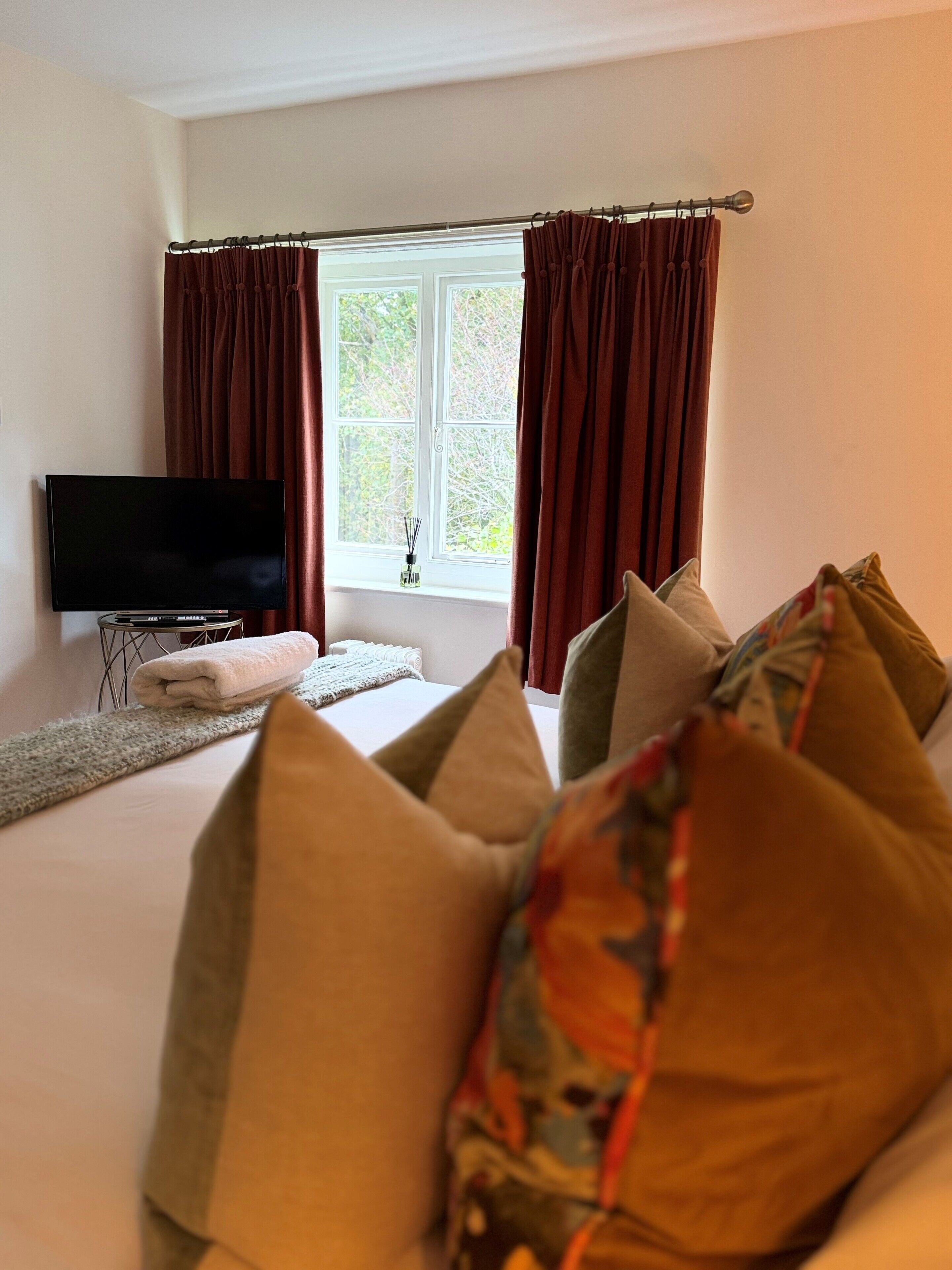 Habitación de hotel con cama, televisor de pantalla plana, ventana con cortinas y vistas a árboles.
