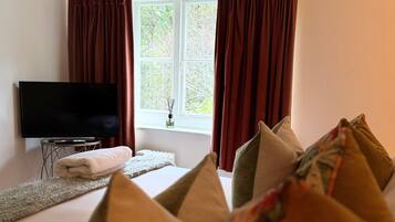 Habitación de hotel con cama, televisor de pantalla plana, ventana con cortinas y vistas a árboles.