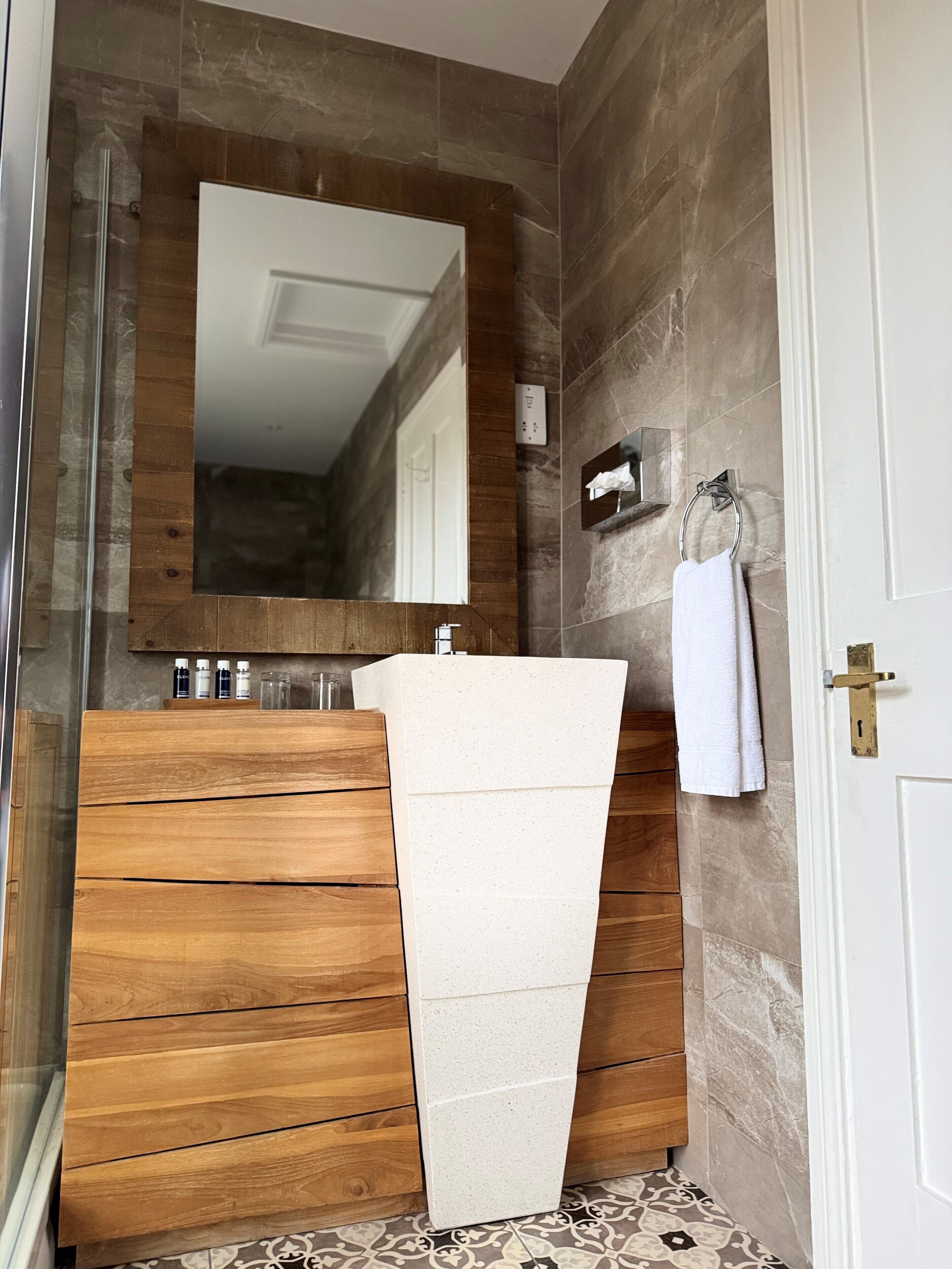 A bathroom with a wooden vanity, a white sink, a large mirror, and a towel hanging on a hook.