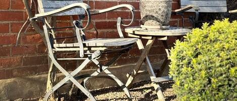 En terrasse med et metalbord og to træstole, en murstensmur og en lille busk.