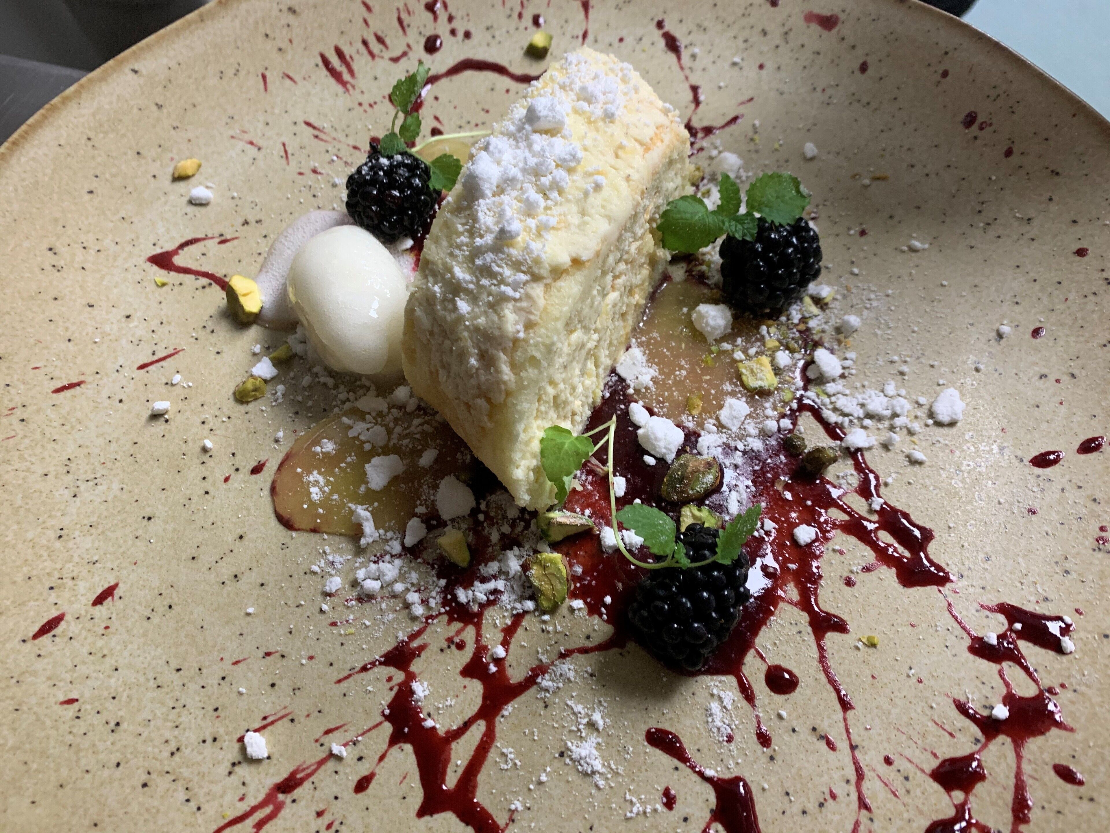 Un dessert composé d’une boule de glace, d’une part de gâteau et de quelques fruits rouges, le tout présenté sur une assiette.