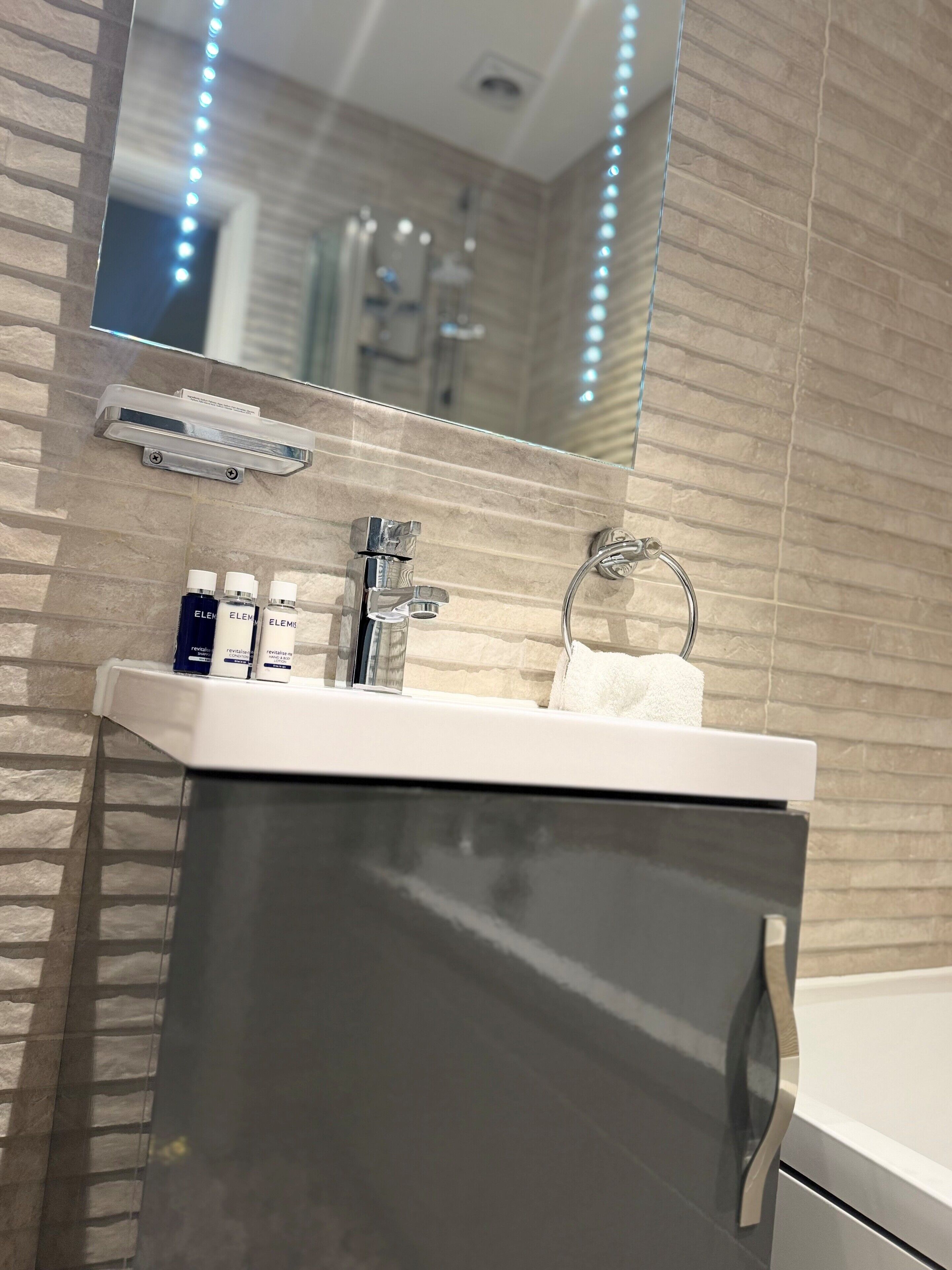 Une salle de bain moderne avec un lavabo blanc, un miroir et un porte-serviettes.