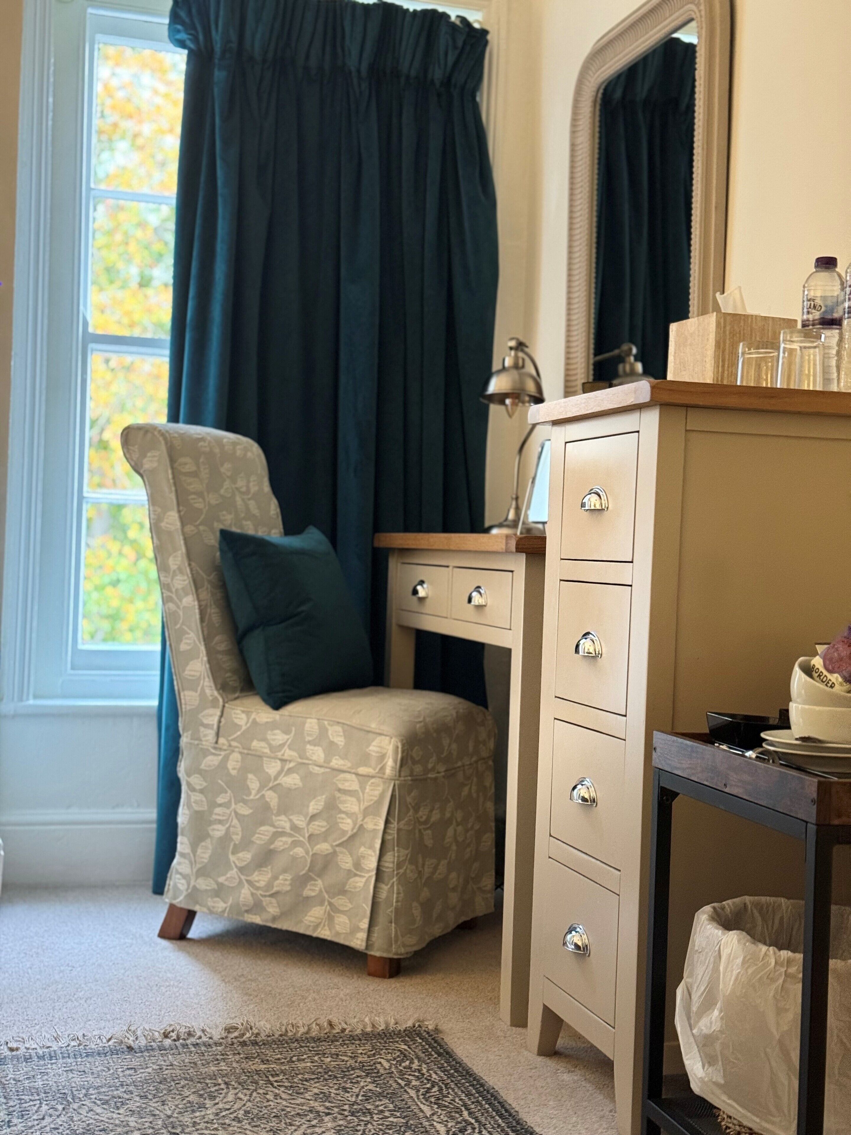 A bedroom with a bed, a chair, a dresser, a mirror, and a window with curtains.