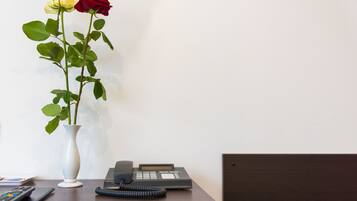 Un bureau avec un téléphone, une télécommande et deux roses dans un vase.