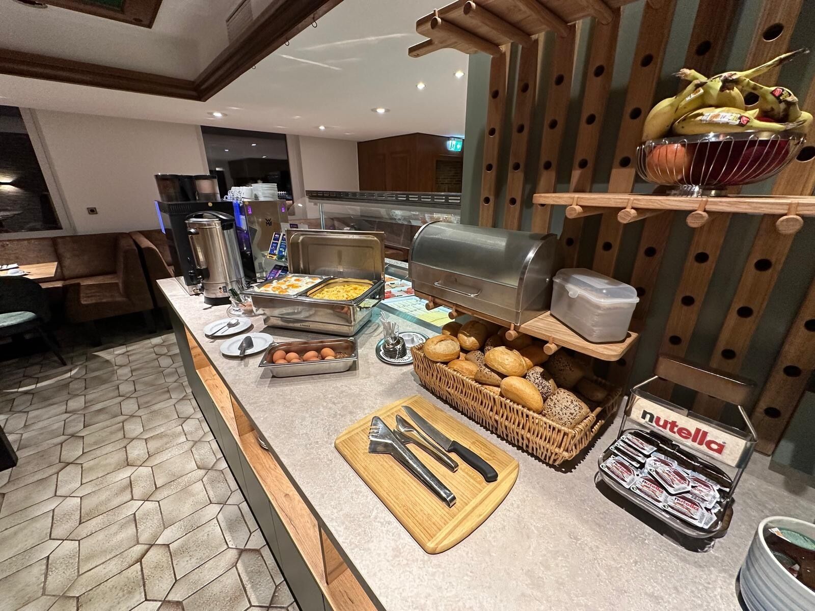 A buffet setup with various food items, a coffee machine, and a Nutella display.