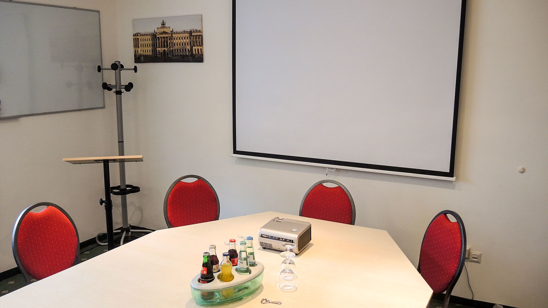 A conference room with a whiteboard, projector, and red chairs.
