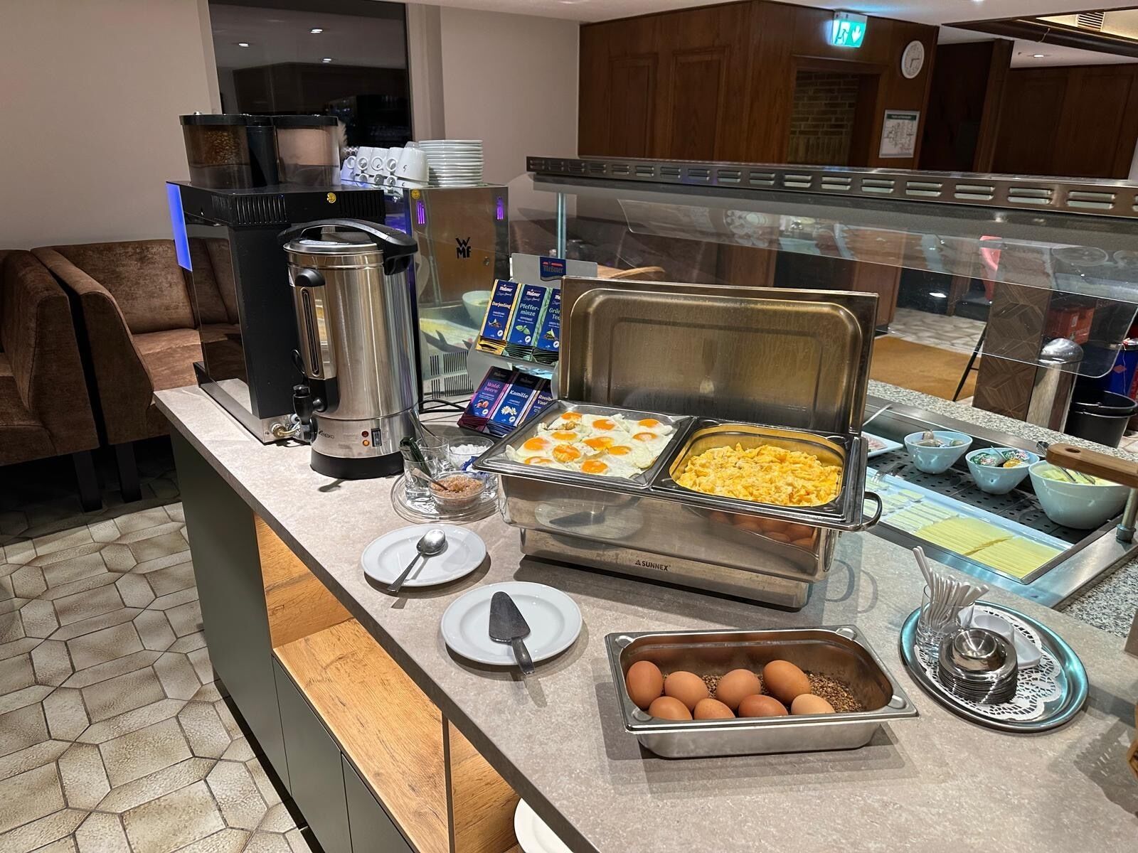 A buffet counter with various food items, a coffee machine, and a glass display case.