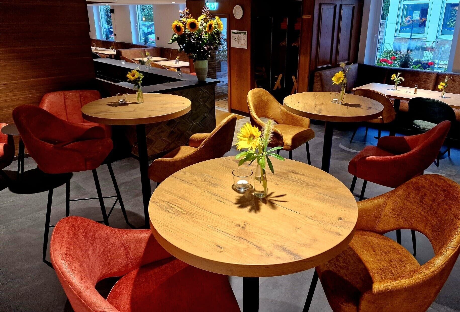 A restaurant with round wooden tables and red chairs, each with a vase of sunflowers.