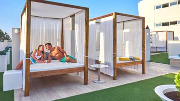 Two wooden canopy beds with white curtains, a small round table, and a potted plant.