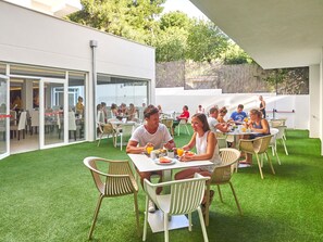 An outdoor dining area with tables and chairs, surrounded by a white building and a grassy lawn. - BQ Bulevar Peguera Hotel - Adults Only (Calvia)