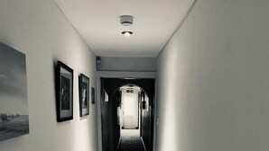 Un couloir étroit au sol carrelé, avec un radiateur sur le côté gauche et des tableaux encadrés accrochés au mur.